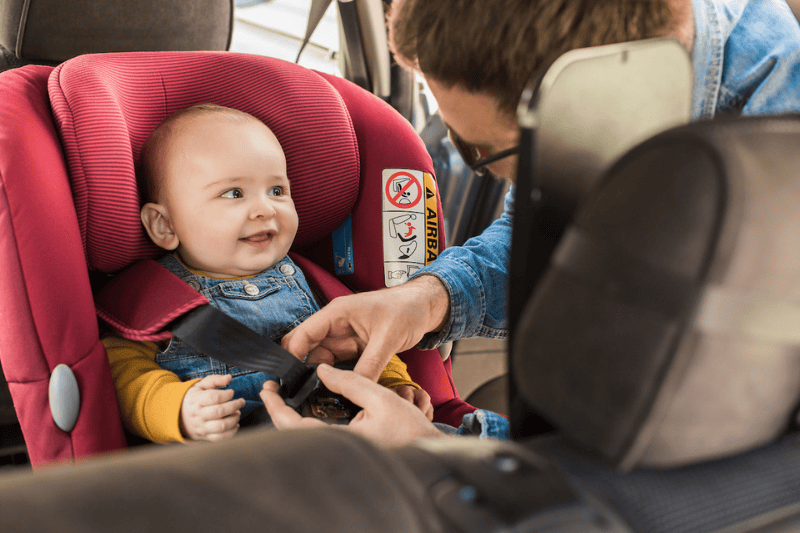 A mother buckles her infant into a car seat