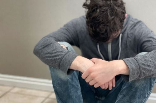 A young man sits sadly