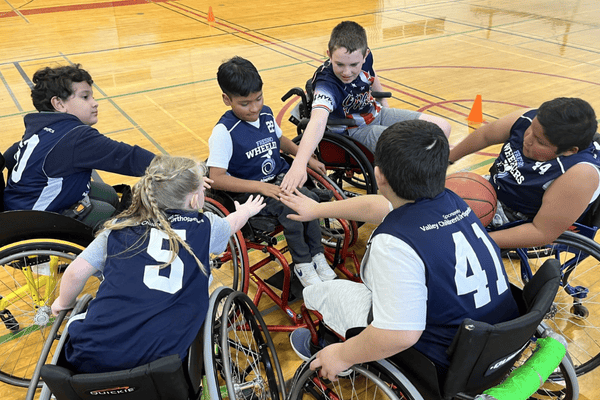 A group of young basketball players in wheelchairs come together for a timeout