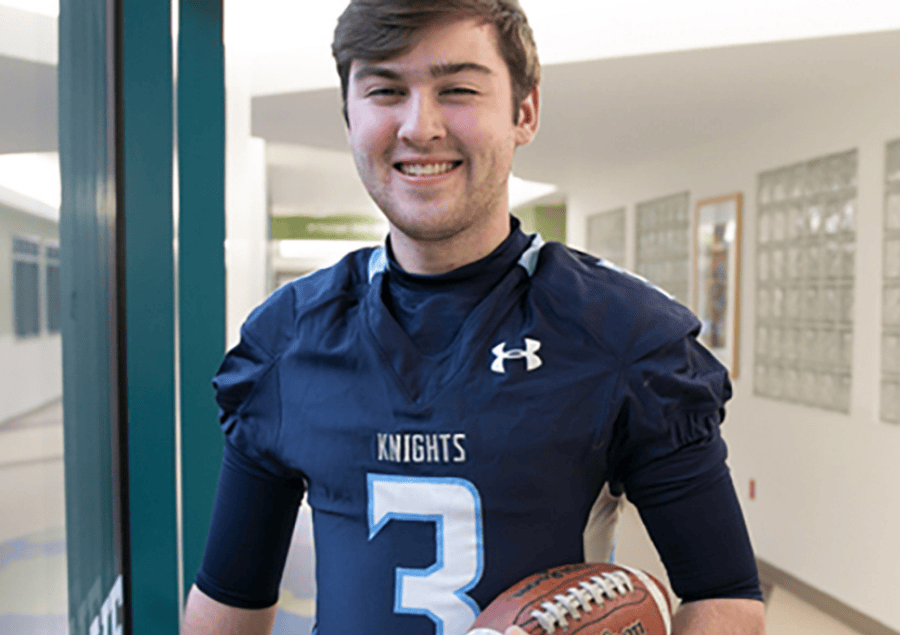 A teenage boy in a football jersey smiles while holding a football