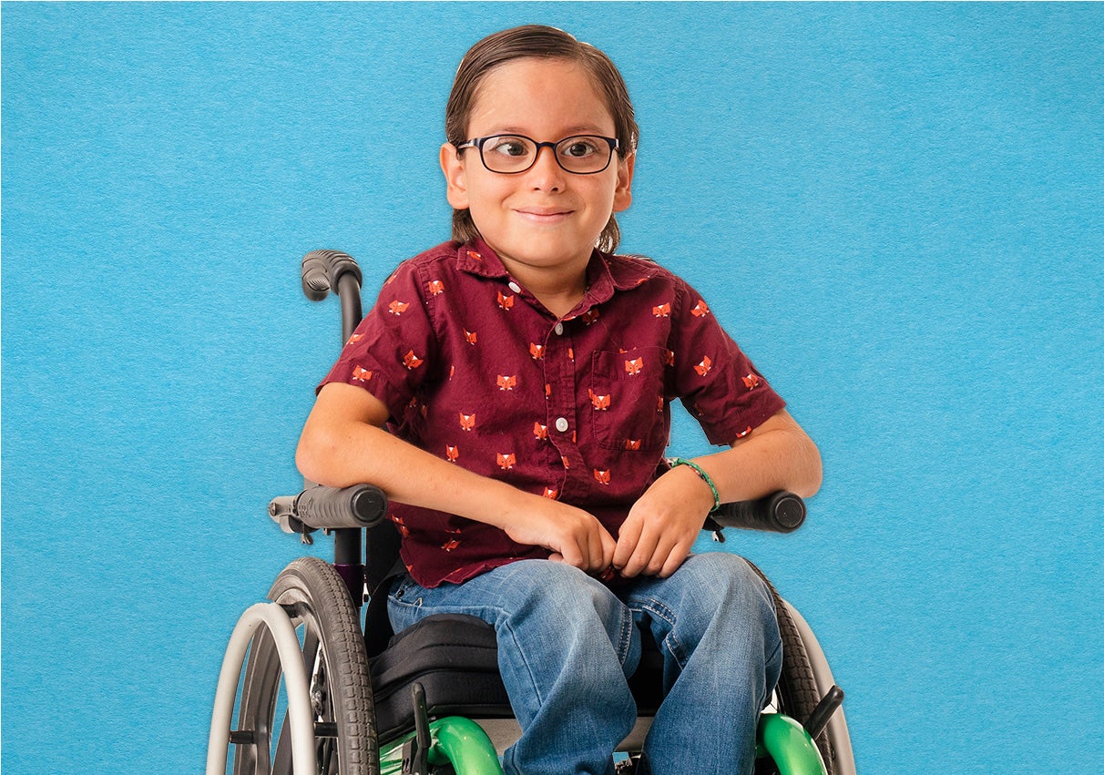 A smiling child with glasses sits in a wheelchair