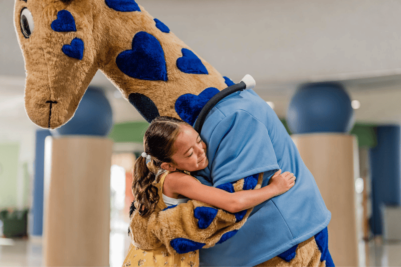 A young girl smiles as she hugs George the Giraffe