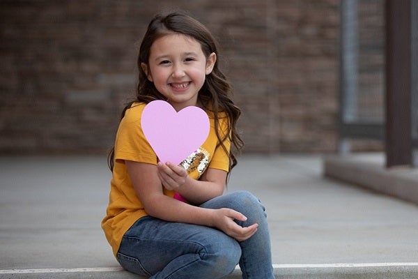 A young girl holds a pink heart shape cutout