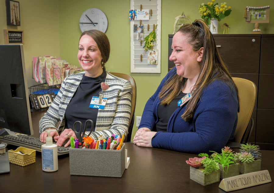 Two nurses work together in front of a computer at a desk