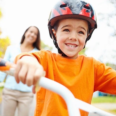 A young boy rides his bicycle while his mother looks on