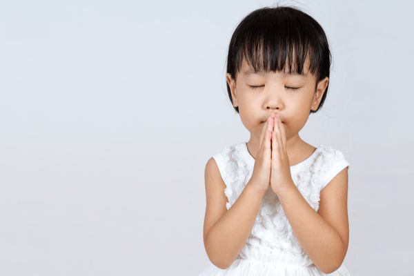 A young girl closes her eyes and prays with her hands together