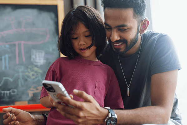 A father and his young daughter look at a smartphone together