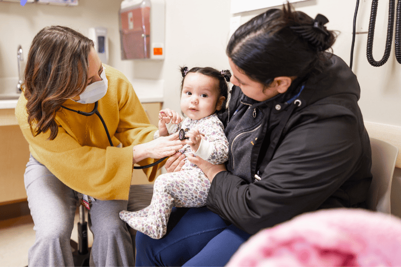 Dr. Erin Vaugh listens through a telescope to the heartbeat of a young patient sitting on her mother's lap