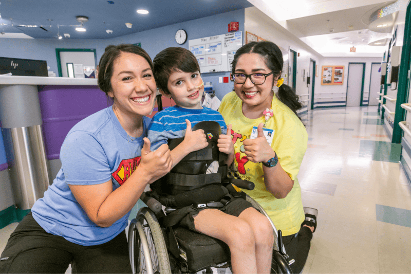 Two Valley Children's pediatric rehabilitation nurses smile with a young patient