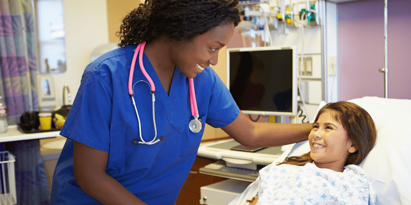 A healthcare provider smiles at a young girl in a hospital bed