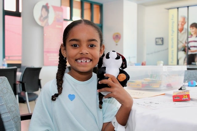 A little girl at Valley Children's smiles while holding a panda plushie