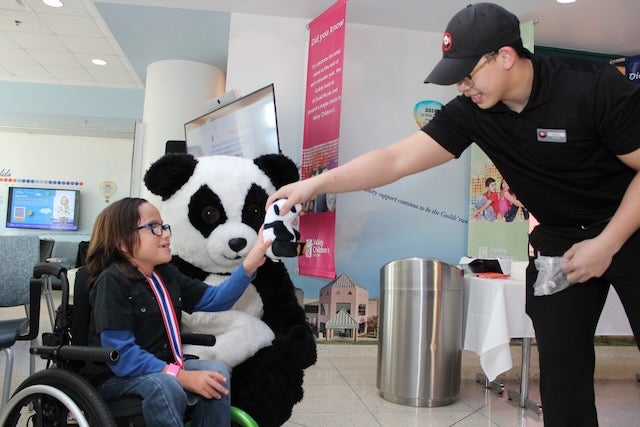 A Panda Express employee gives a toy to Sylus, 2024 CMN Champion patient