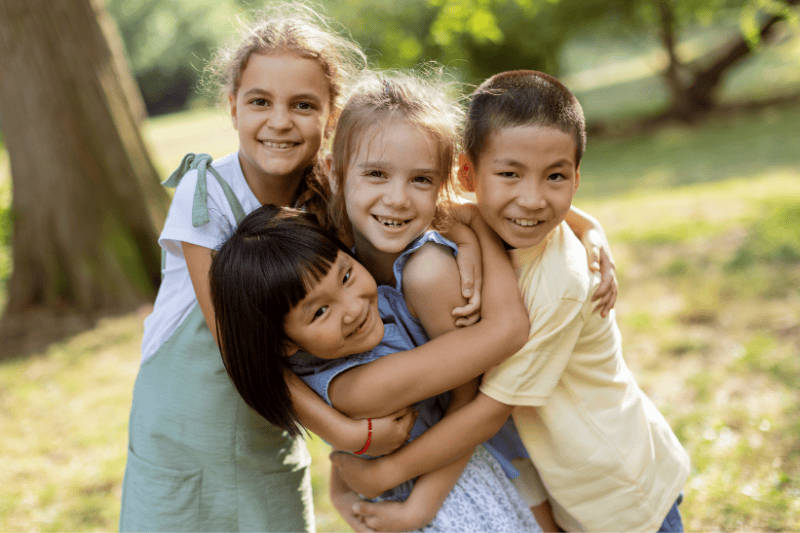 A group of four young children hug