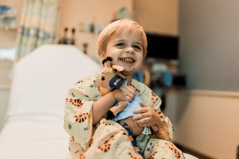 A young boy smiles as he holds a stuffed giraffe
