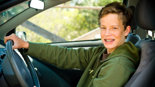 Teen boy sitting behind wheel of a car smiling