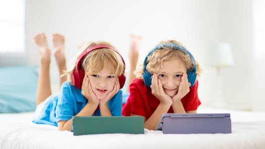 Two children laying down with tablets and headphones