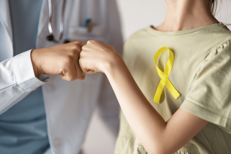 A doctor and young girl wearing a childhood cancer awareness ribbon fist bump