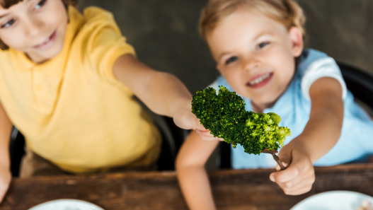 Children holding forks into the air with broccoli on them