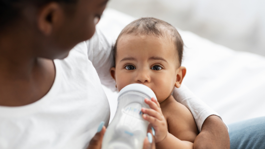 Child taking a bottle in their mother's arms