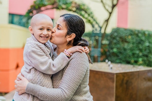 A young girl smiles as her mother kisses her on the cheek